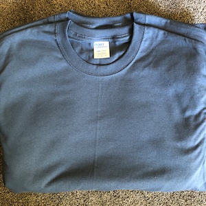 May include: A folded dark blue t-shirt with a white tag that reads "Port Company" and "100% Cotton" in a black font.