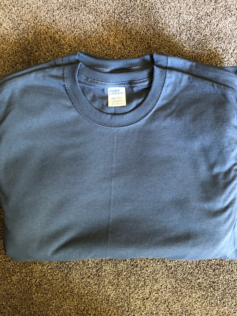 May include: A folded dark blue t-shirt with a white tag that reads "Port Company" and "100% Cotton" in a black font.