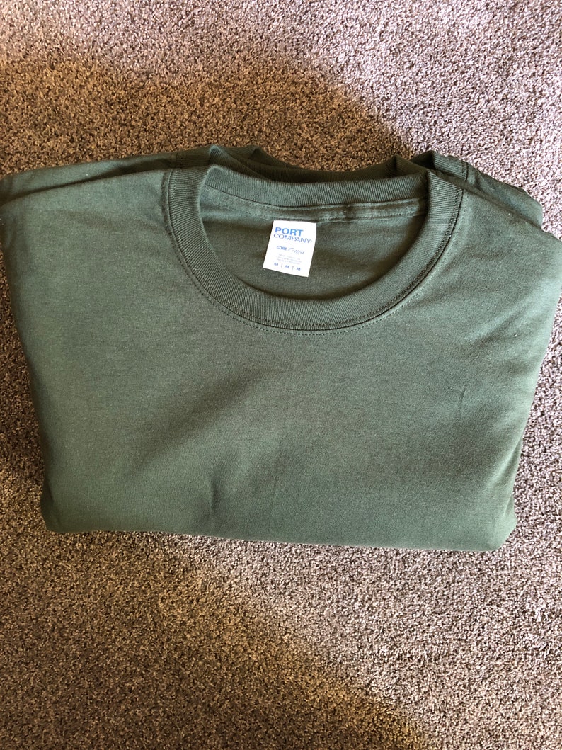 May include: A folded green long-sleeved t-shirt with a white tag that reads "PORT COMPANY" and "COMFORT COLORS" with the size "M" printed on it.