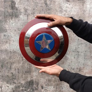 May include: A circular shield in red, white, and blue, featuring a star emblem. The shield has a silver band separating the red outer ring from the blue center. A silver star is in the center.