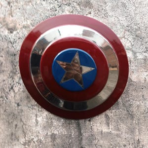 May include: A circular shield featuring a red outer ring, a silver band, and a blue central disc with a gold star. This shield is a replica of a famous superhero's emblem.