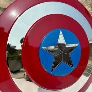 K&ouml;nnte beinhalten: Ein rot, wei&szlig; und blaues Schild mit einem Sternemblem. Das Schild hat einen gl&auml;nzenden, reflektierenden silbernen Ring und eine blaue Mitte mit einem silbernen Stern. Der &auml;u&szlig;ere Ring ist rot, und das Schild scheint aus Metall zu sein.