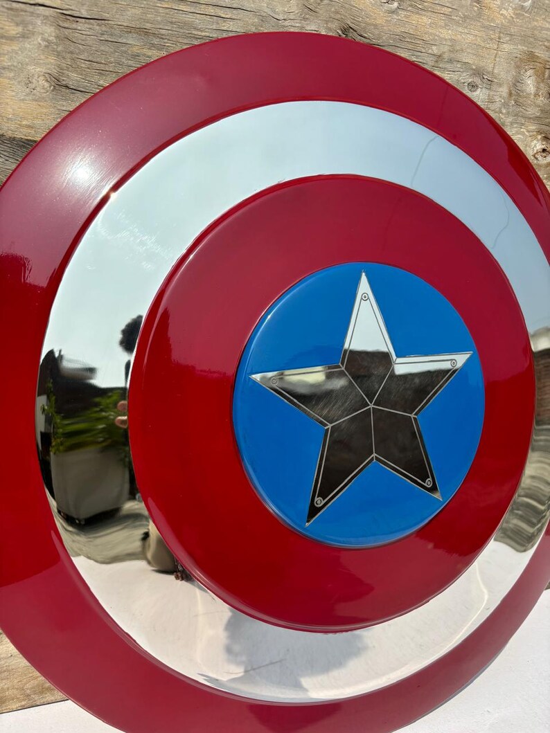 K&ouml;nnte beinhalten: Ein rot, wei&szlig; und blaues Schild mit einem Sternemblem. Das Schild hat einen gl&auml;nzenden, reflektierenden silbernen Ring und eine blaue Mitte mit einem silbernen Stern. Der &auml;u&szlig;ere Ring ist rot, und das Schild scheint aus Metall zu sein.