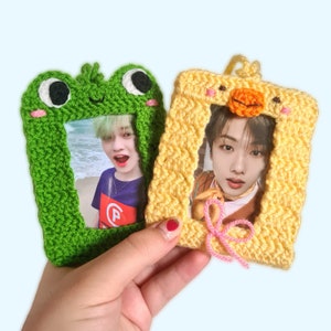 Può includere: Due cornici per foto all'uncinetto, una verde e una gialla, con un design a forma di rana e pulcino. Ogni cornice contiene una foto di una persona.