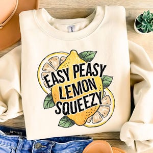 Puede incluir: Una sudadera de color crema con un gráfico de un limón y el texto "Easy Peasy Lemon Squeezy".