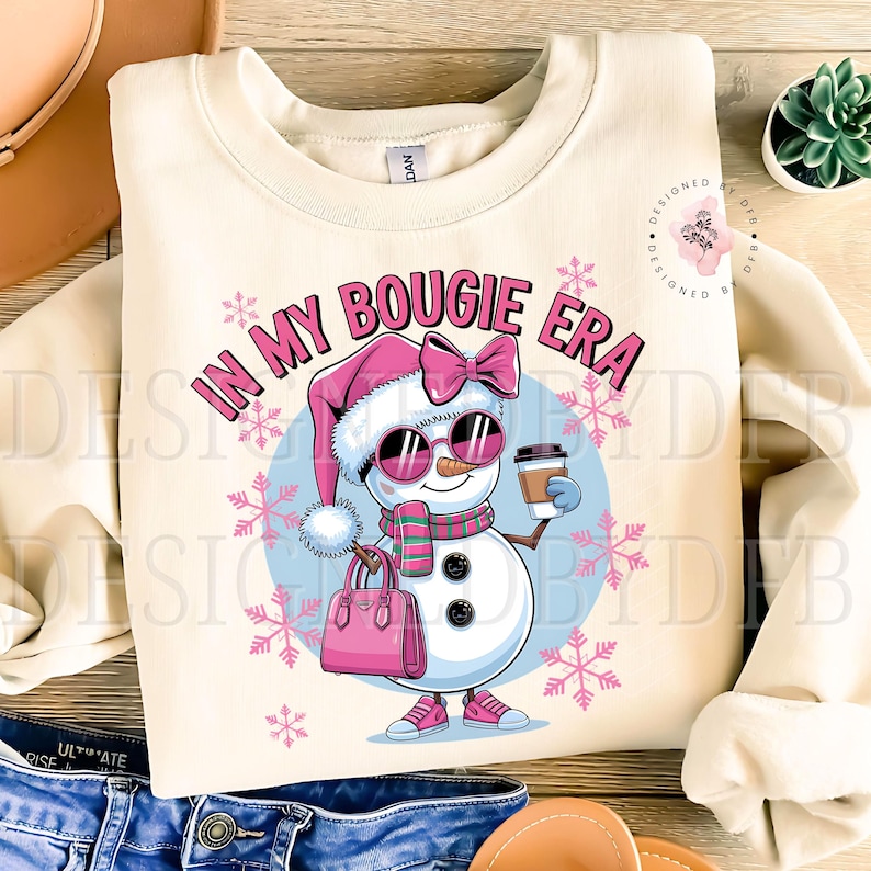 May include: A cream-colored sweatshirt with a snowman wearing sunglasses, a pink hat, and a pink bow. The snowman is holding a cup of coffee and a pink purse. The text "In My Bougie Era" is printed on the sweatshirt.