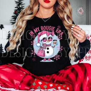 May include: Black sweatshirt with a pink and white snowman wearing sunglasses and holding a coffee cup. The snowman is holding a pink purse and the text "In My Bougie Era" is above the snowman.
