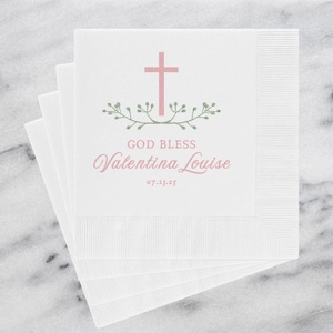 May include: White paper napkins with a pink cross and green leaves design. The text reads "God Bless Valentina Louise 07.13.25".