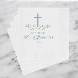 May include: White paper napkins with a blue cross and green leaves design. The text "God Bless Max Alexander 07.13.25" is printed on the napkins.