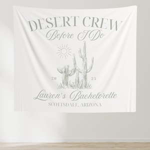 May include: White backdrop with the text "Desert Crew Before I Do" in green lettering.  Below the text is a drawing of three cacti and a sun.  The text "Lauren's Bachelorette Scottsdale, Arizona" is below the cacti.