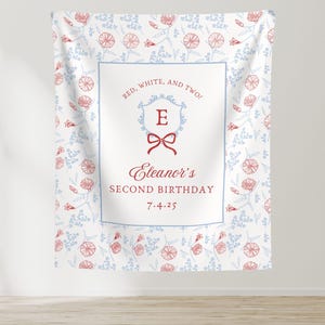 May include: A white backdrop with a floral pattern in red and light blue. The center features a blue-bordered rectangle with text: "RED, WHITE, AND TWO!" and "Eleanor's SECOND BIRTHDAY 7.4.25". A red bow and the letter "E" are also present.