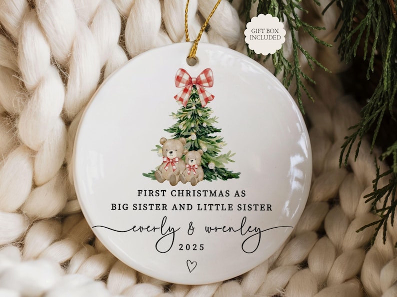 May include: A white ceramic Christmas ornament with a watercolor design. It features a Christmas tree, two teddy bears, and a red and white plaid bow. Text reads "First Christmas as Big Sister and Little Sister" with names and the year 2025.