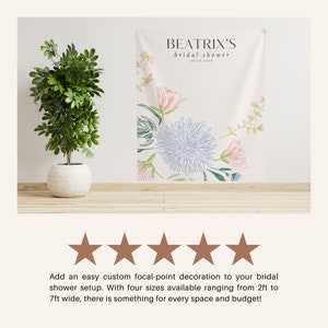 May include: A white backdrop with a floral design in shades of blue, pink, and green. The text "BEATRIX'S bridal shower 06.17.20XX" is printed at the top of the backdrop.