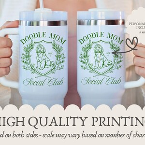 May include: Two white travel mugs with the text "DOODLE MOM Social Club" in green. Each mug features a doodle dog illustration within a green floral crest. The mugs have white handles and silver rims.