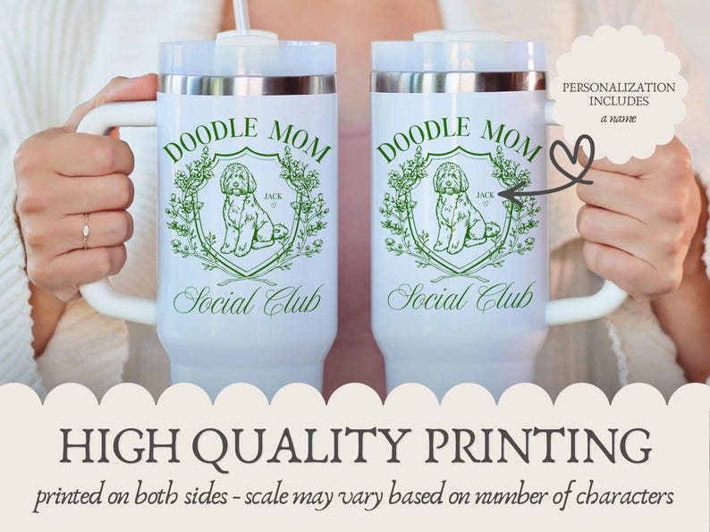 May include: Two white travel mugs with the text "DOODLE MOM Social Club" in green. Each mug features a doodle dog illustration within a green floral crest. The mugs have white handles and silver rims.