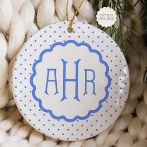May include: A round white ceramic ornament featuring a blue polka dot pattern and a central scalloped frame containing the blue monogram letters AHR. The ornament hangs from a gold string and includes a small white label stating GIFT BOX INCLUDED.