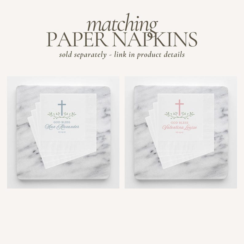 May include: Two white paper napkins with a cross and floral design. The text "God Bless" is printed on each napkin, along with a name. One napkin has a blue cross and the name "Max Alexander". The other napkin has a pink cross and the name "Valentina Louise".