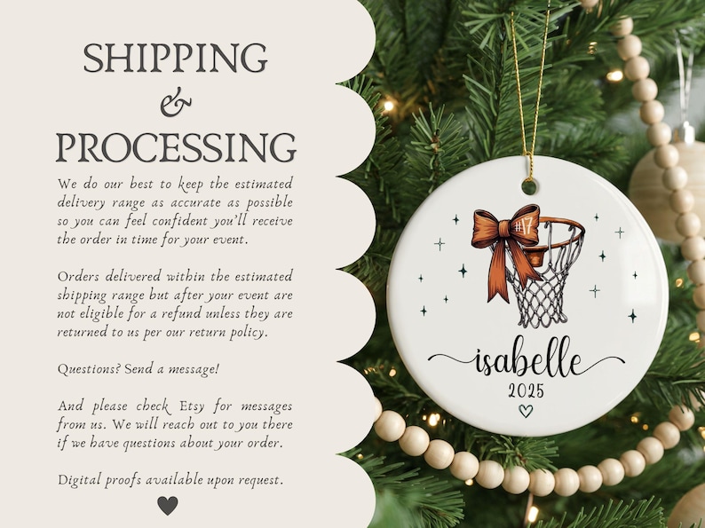 May include: A white ceramic Christmas ornament with a basketball hoop design and a decorative orange bow. The ornament includes the name "isabelle", the year "2025", and a heart symbol. It hangs from a gold string.