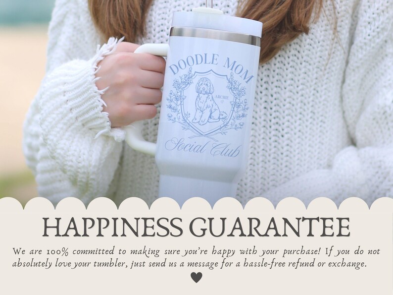 May include: A white tumbler with a handle, featuring the text "DOODLE MOM Social Club" and a doodle dog illustration in blue. The tumbler is held by a person wearing a white sweater. The bottom of the image has the text "HAPPINESS GUARANTEE".