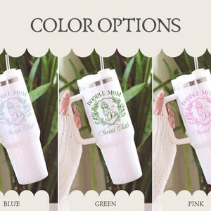 May include: White insulated tumbler with a handle, featuring the text "DOODLE MOM Social Club" in blue, green, and pink. The tumbler has a silver lid and a straw. The image shows three color options: blue, green, and pink.