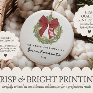 May include: A round white ceramic ornament featuring a green watercolor wreath with a red bow. The bow has the name Eliana printed on it. Below the wreath, the text reads Our First Christmas as Grandparents 2025 in black lettering.