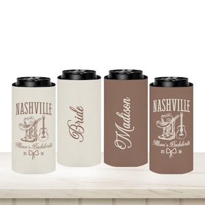 May include: Four slim can coolers with black tops. Two are tan, one is brown, and one is a darker brown. Text includes "Nashville", "Bride", and "Madison". The Nashville coolers have a cowboy boot, hat, and guitar graphic.