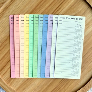 May include: A collection of colorful book trackers. Each tracker is a different pastel color, with lines for the book title, name, and rating. The text "Books I've Read in 2026" is printed on one of the trackers.