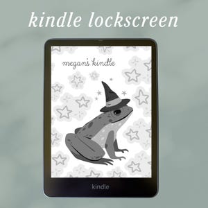 May include: A Kindle e-reader displaying a custom lockscreen. The lockscreen features a gray frog wearing a witch hat, with the text "megan's kindle" and "kindle." The background has a pattern of stars and clouds.