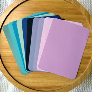 May include: A collection of colorful rectangular cards in shades of blue, green, and purple, arranged in a fan shape. The cards are on a wooden tray, creating a visually appealing display of color swatches.