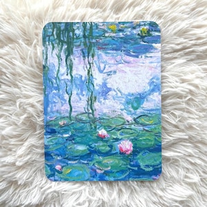 May include: A rectangular art print featuring a water lily pond scene in shades of blue, green, and pink. The artwork depicts lily pads, water, and flowers, with a soft, impressionistic style. The print is set against a fluffy, white background.