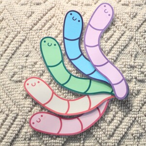 May include: Four colorful worm stickers with happy faces. The worms are pink, blue, green, and white.