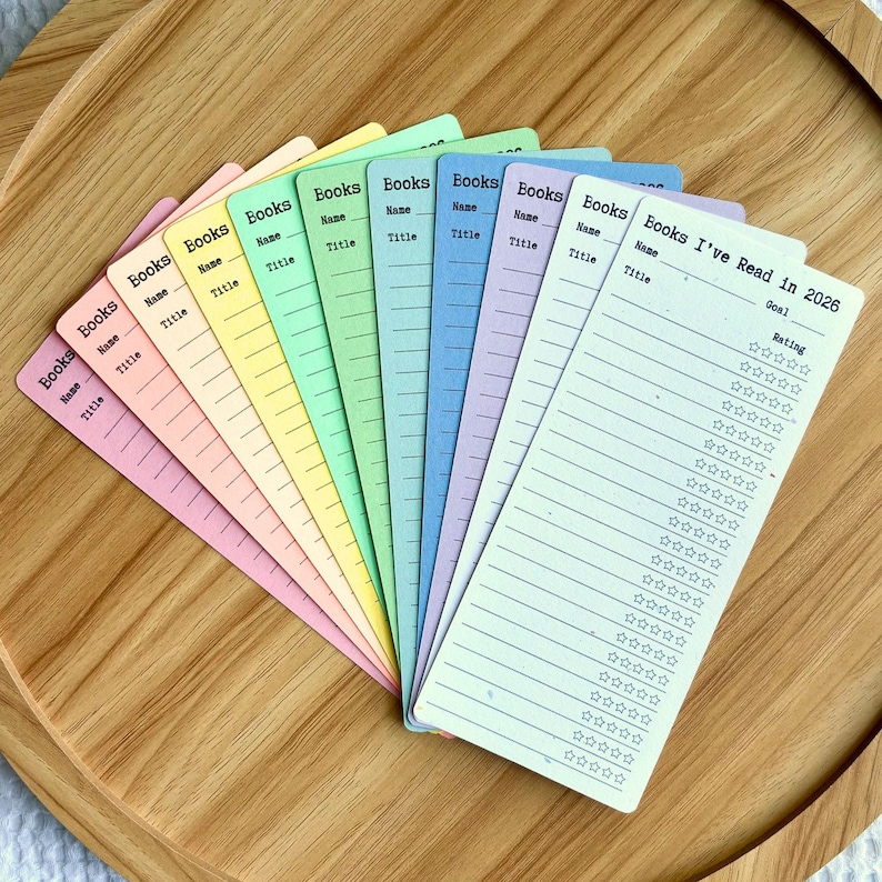 May include: A collection of colorful book trackers in pastel shades, arranged on a wooden tray. Each bookmark features the word "Books", space for the name and title, and a section for rating. One bookmark reads "Books I've Read in 2026".