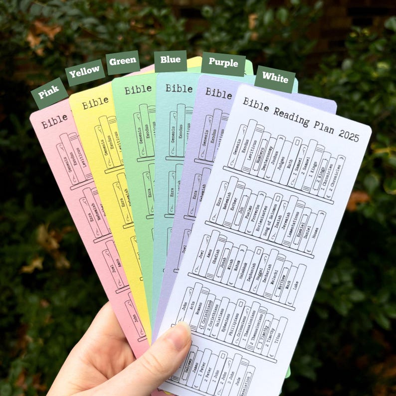 May include: A set of six colorful bookmarks with a Bible reading plan for 2025. Each bookmark features a bookshelf with different books of the Bible listed in order. The bookmarks are labeled with the colors pink, yellow, green, blue, purple, and white.
