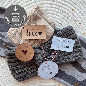 Puede incluir: Primer plano de tres diademas hechas a mano en tonos neutros. Una es beige y dos son grises. Cada diadema tiene una etiqueta que dice "Handmade with love" o "Handarbeit mit Liebe". Las diademas están sobre una superficie estampada.