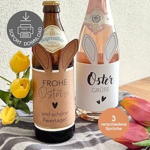 Puede incluir: Dos botellas decoradas para Pascua, una de cerveza y otra de rosado. La botella de cerveza tiene orejas de conejo marrones y una etiqueta con texto en alemán. La botella de rosado tiene orejas de conejo y una etiqueta con el texto "Oster GRÜBE".