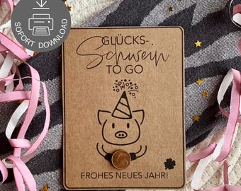 May include: A brown card with the text "GLÜCKS-SCHWEIN TO GO" and "FROHES NEUES JAHR!" features a cartoon pig wearing a party hat. A coin is placed below the pig. Pink ribbons and gold stars are scattered around the card.