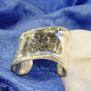 May include: A silver hammered cuff bracelet with a rounded shape. The bracelet has a textured surface and is marked with "OSE 116".