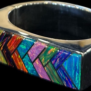 Op de afbeelding: Een zilveren ring met een rechthoekige inleg van iriserende opaal mozaïektegels in een geometrisch patroon.