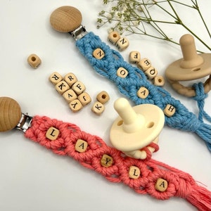 May include: Three handmade baby teethers with wooden beads spelling out the names "Layla", "Noah", and "Kay", each with a wooden clip and a silicone pacifier.
