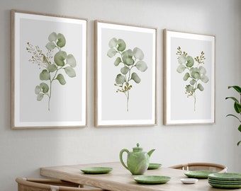 May include: A dining room with a wooden table and chairs, featuring a light green and white color scheme. Three framed botanical prints with green leaves hang on the wall. The room has a large window with white curtains and a view of green trees.
