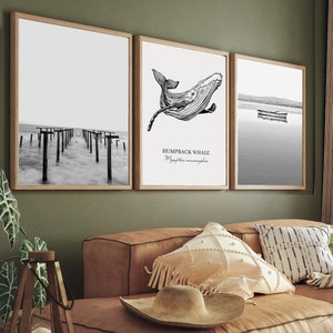 Może przedstawiać: Salon z brązową skórzaną sofą narożną, stolikiem kawowym z książkami i wazą z kwiatami oraz trzema czarno-białymi obrazami w ramach na ścianie. Obrazy przedstawiają wieloryba garbatego, pomost i jezioro z łodzią.