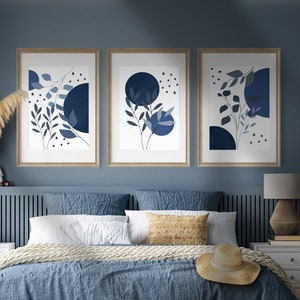 Peut inclure: Une chambre à coucher bleue avec un lit, une tête de lit et trois impressions encadrées avec des motifs abstraits bleus et blancs. Le lit a une couette bleue, une couverture blanche et un oreiller beige. Il y a un chapeau de paille sur le lit.