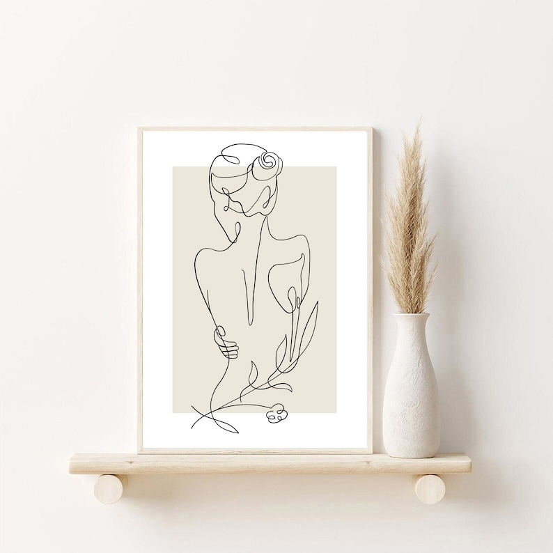 May include: Line art print of a nude figure with a flower in their hair, standing with their back to the viewer. The figure is outlined in black against a beige background.