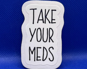 May include: A white die-cut sticker with a wavy, irregular border featuring the black hand-lettered text "TAKE YOUR MEDS" stacked in three lines. The sticker has a clean, simple design with a matte finish and a distinct, organic shape.