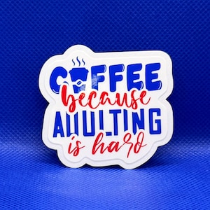 May include: A die-cut sticker with a white background featuring the blue text COFFEE and ADULTING in a bold sans-serif font, with the red script text because and is hard. A small blue coffee cup icon is integrated into the word COFFEE.