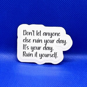 May include: A white sticker with a black border and text that reads, "Don't let anyone else ruin your day. It's your day. Ruin it yourself." The sticker is on a blue background.