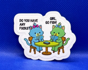 May include: A die-cut sticker featuring a blue cat and a green cat sitting at a round table playing cards. The blue cat has a pink bow and the green cat has a blue bow. Text bubbles read: DO YOU HAVE ANY FUCKS? and GIRL, GO FISH!
