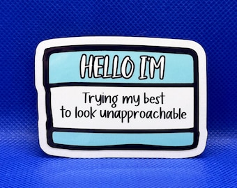 May include: A rectangular sticker designed like a name tag with a light blue border and white center. The text HELLO I'M is printed in black at the top, followed by the text Trying my best to look unapproachable in black lettering in the center.