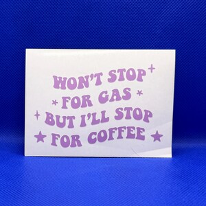 May include: A white square sticker with the text "WON'T STOP FOR GAS BUT I'LL STOP FOR COFFEE" in lavender. The text is in a retro font with star and plus symbols. The sticker is against a blue background.
