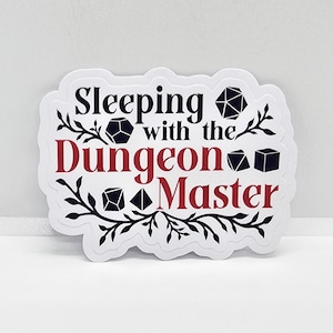 May include: White sticker with black and red text that reads "Sleeping with the Dungeon Master". The sticker features a black and white floral design with several black dice.